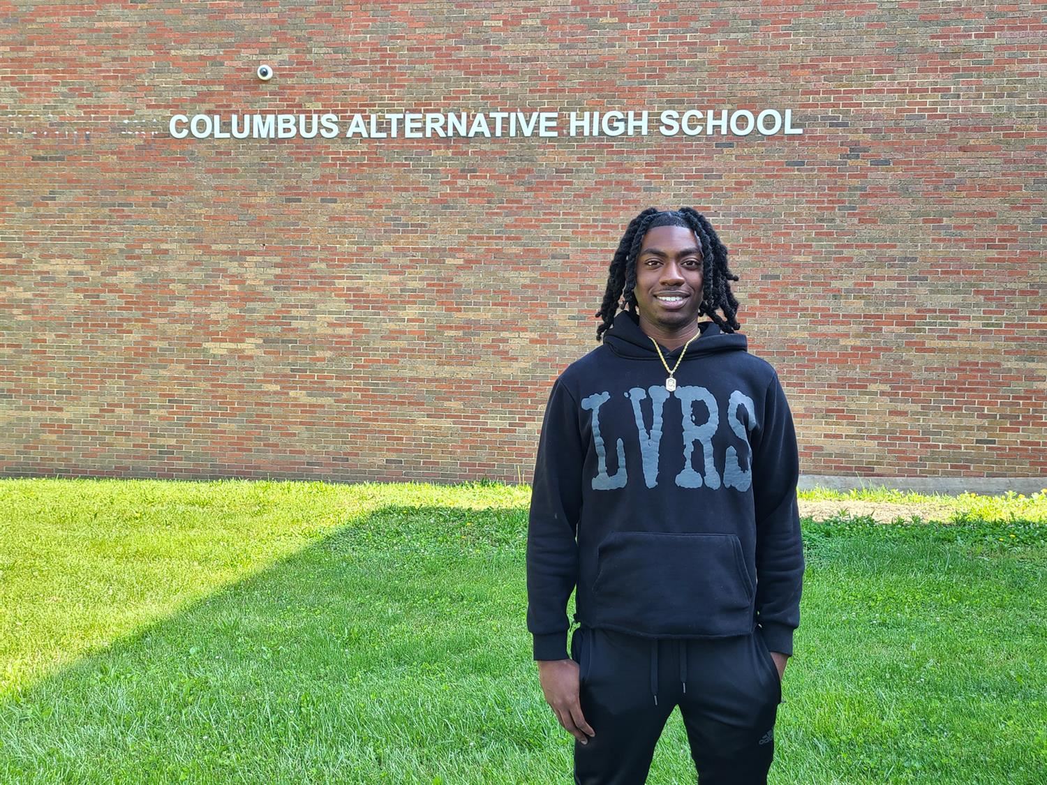student dressed in black standing in front of brick building