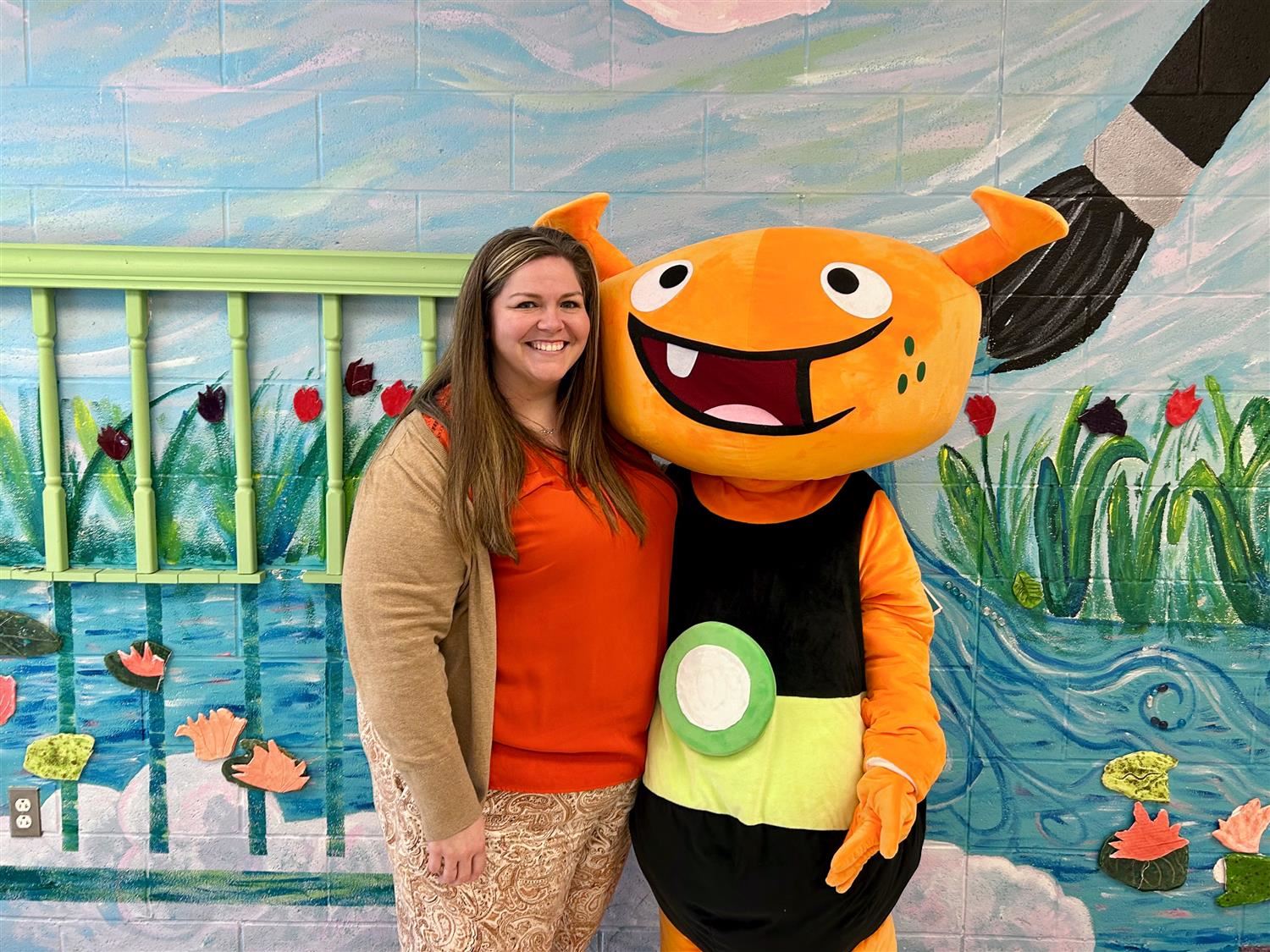 Principal posing with arm wrapped around friendly orange monster