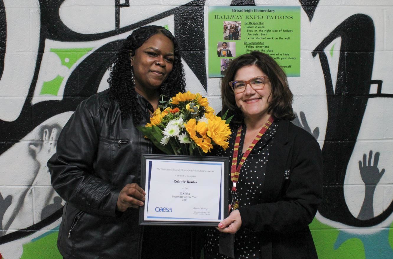 women holding plaque and flowers together