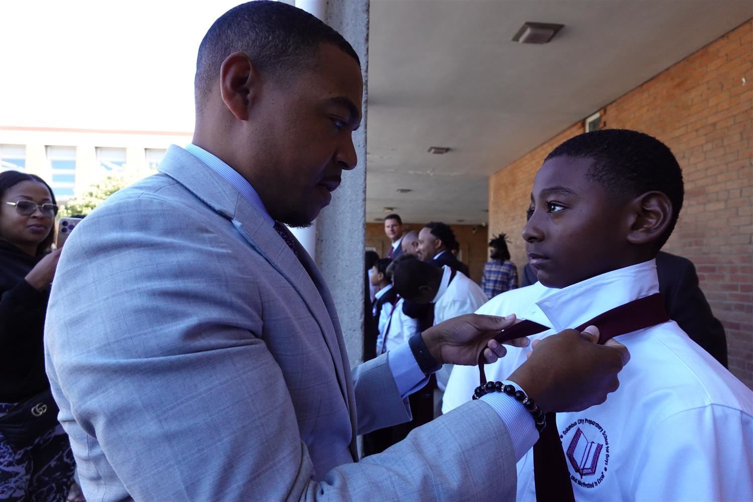 adult tying the neck tie of a young student