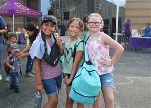 three students holding backpacks smiling at camera