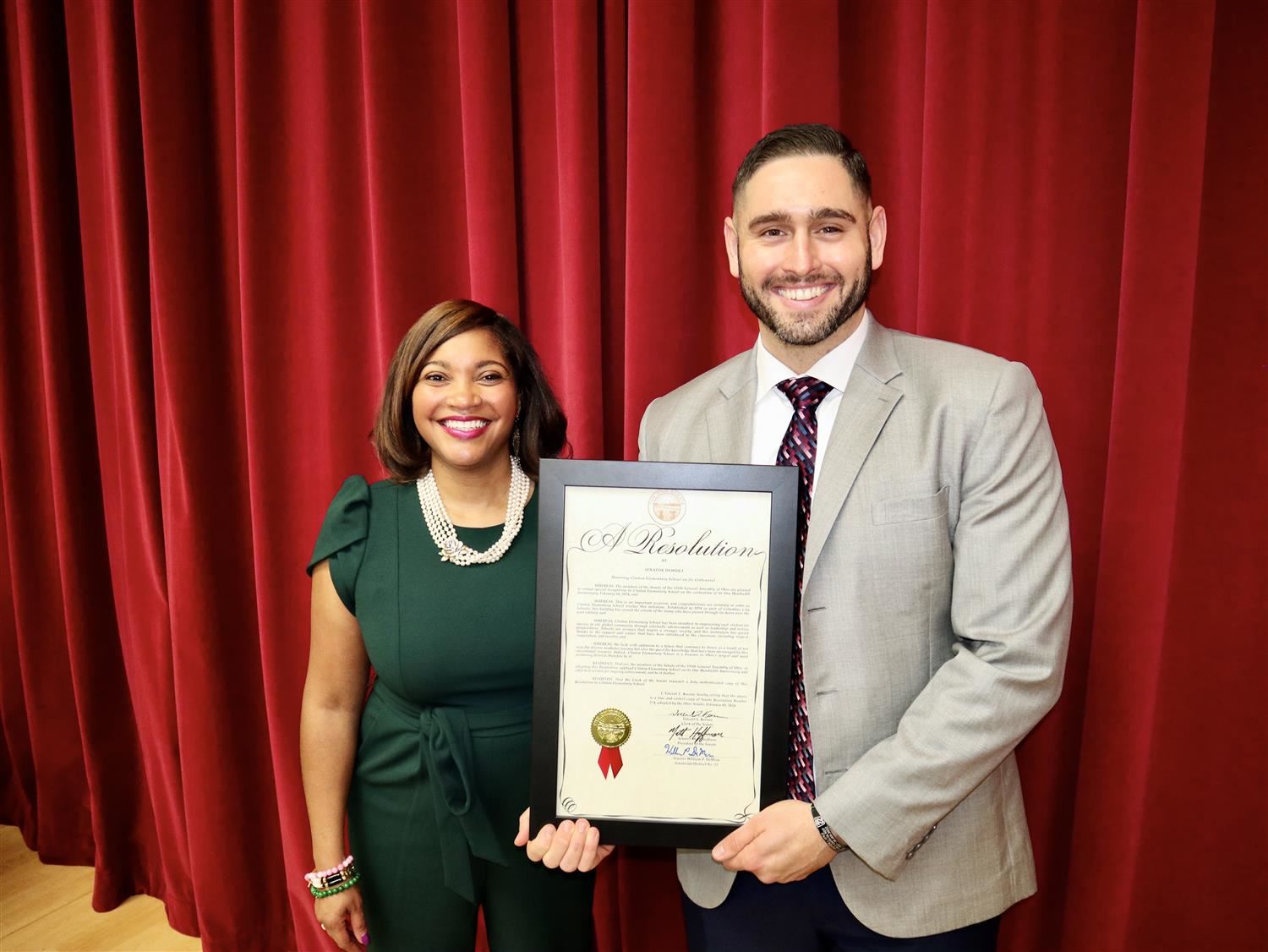 woman dressed in green standing next to man in suite holding a plaque