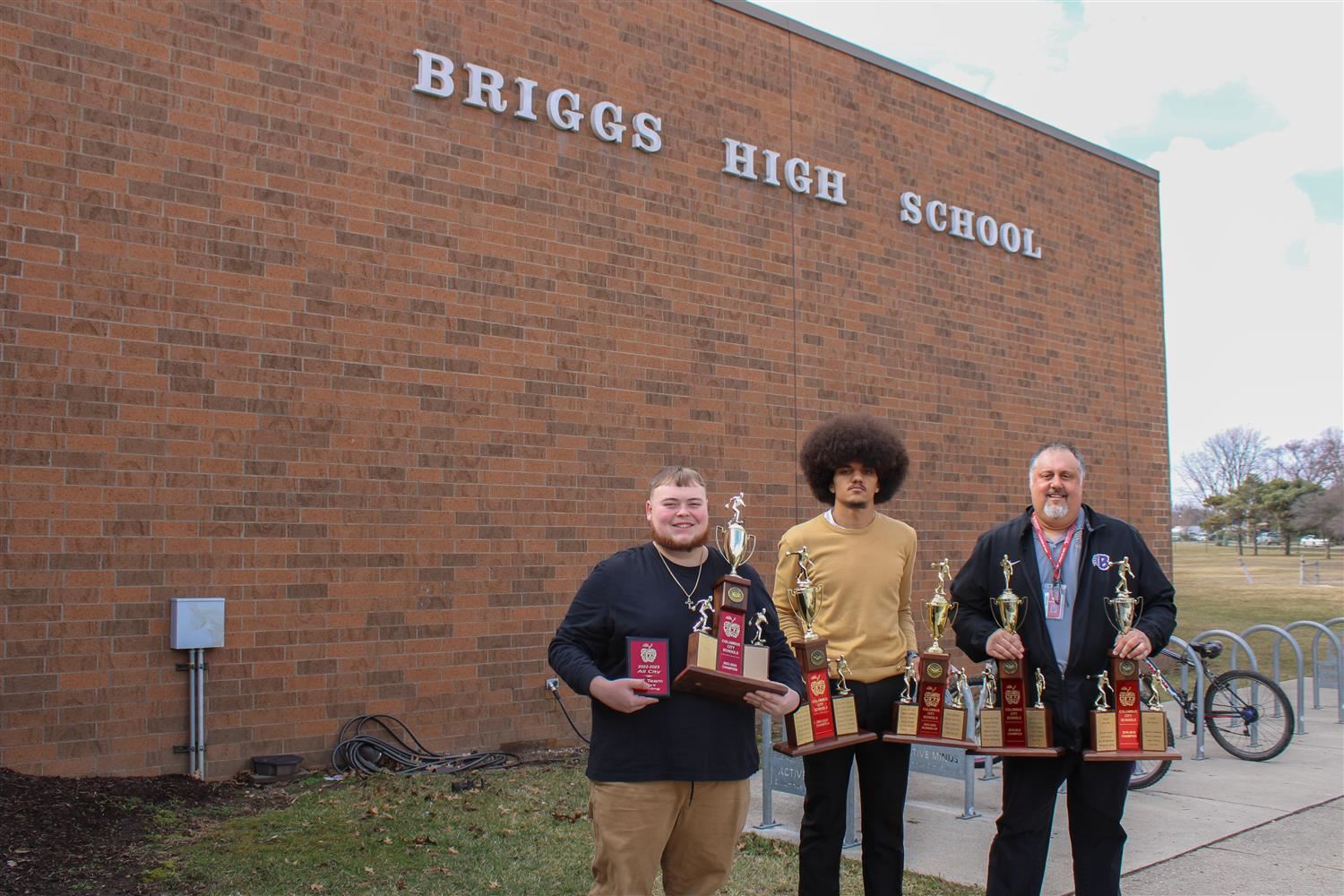 two students and a coach each holding two trophies