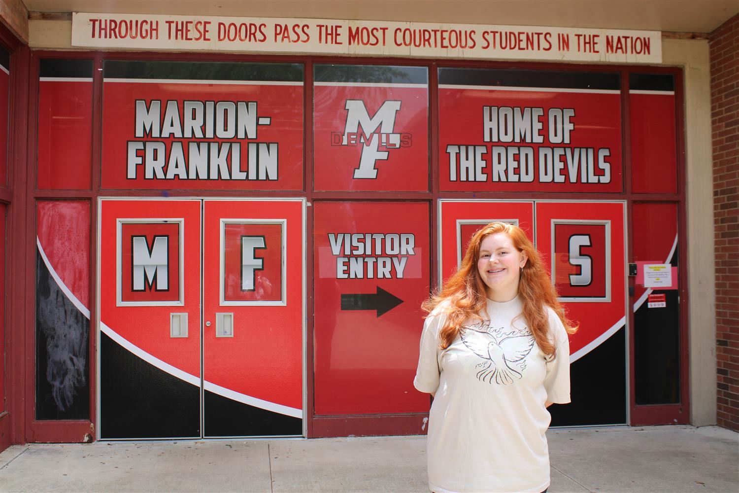girl standing in front of red doors that read Marion Franklin High School