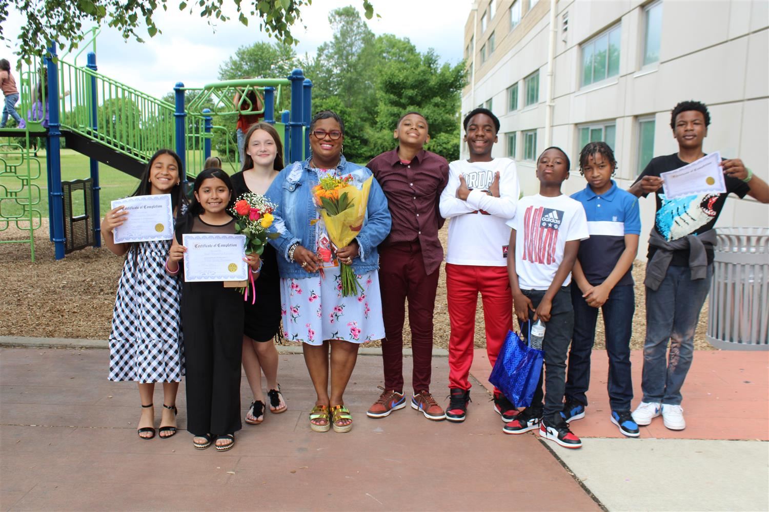 student posing on playground surrounded by students holding certificates